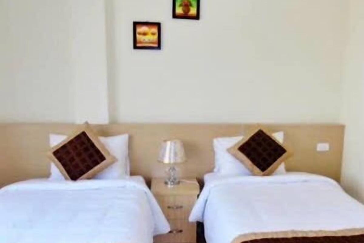 A hotel room with two beds, each with a pillow and a small table with a lamp.