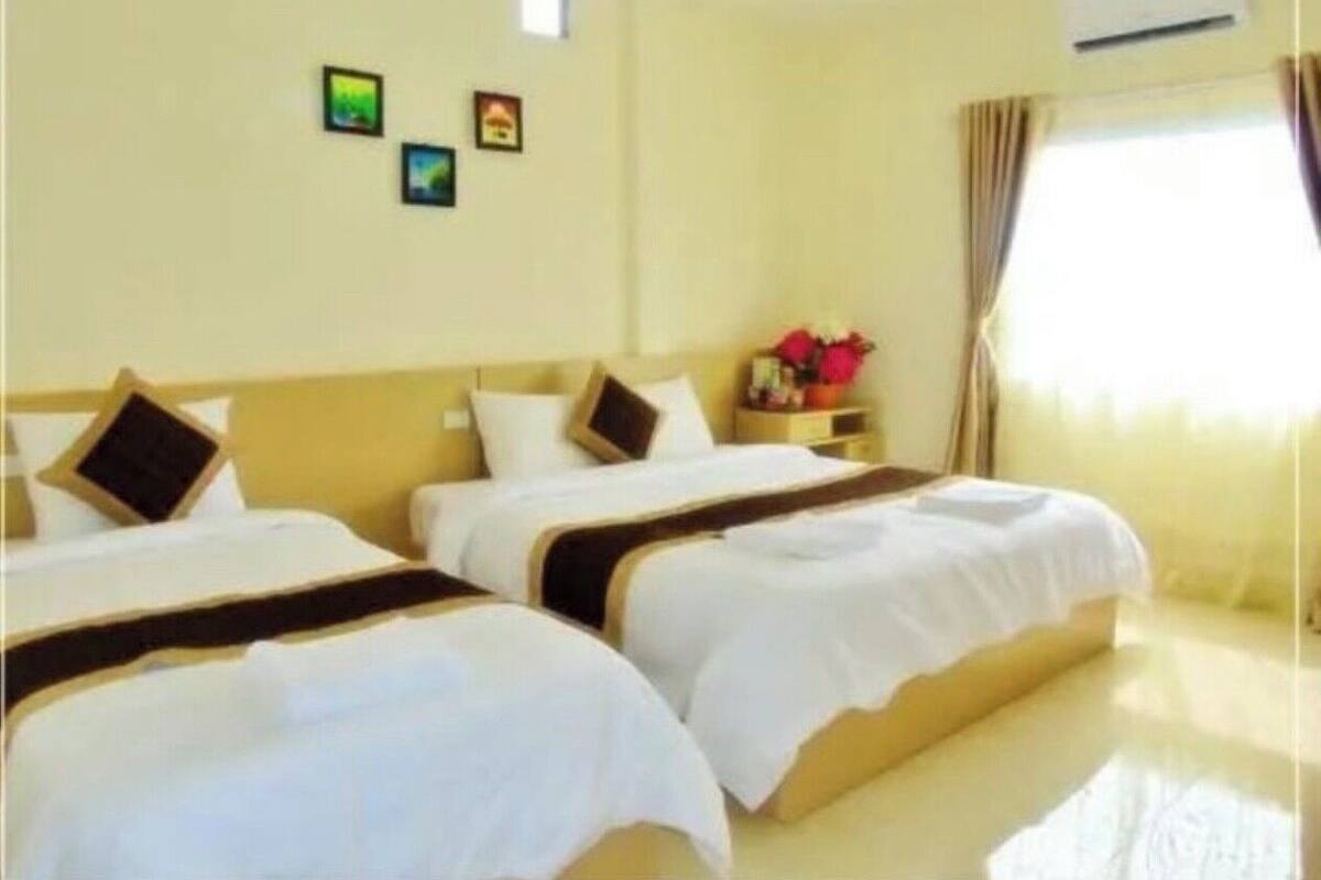 A hotel room with two beds, a nightstand, a small table with a vase, and a window with curtains.