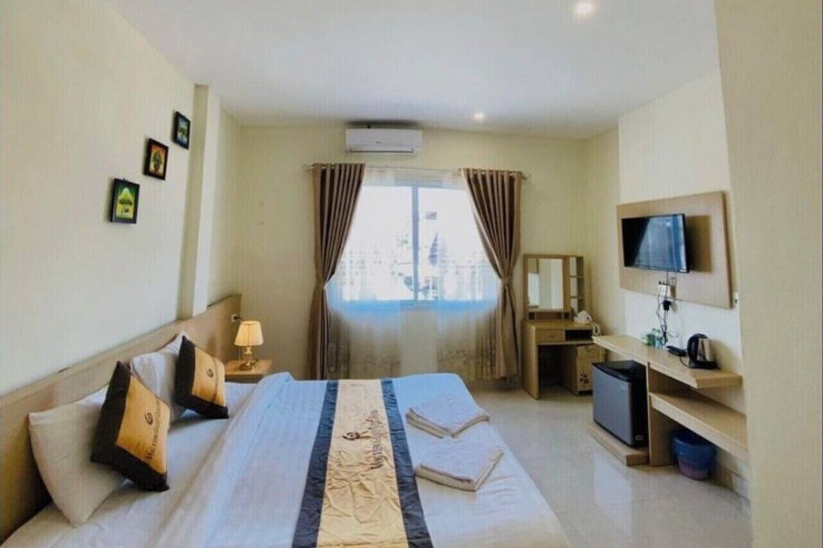 A hotel room with a bed, a desk, a TV, and a window with curtains.