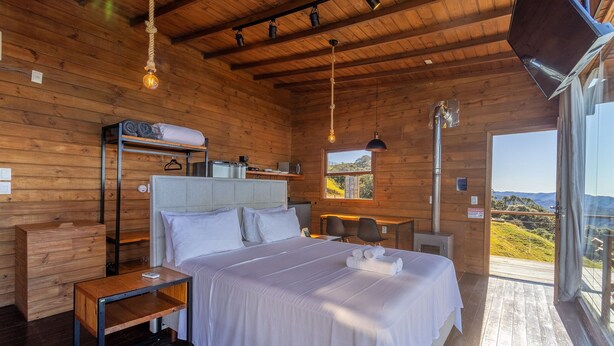 A wooden cabin bedroom with a bed, bedside tables, a desk, and a window with a view. - Linda cabana com jacuzzi VST004 (Anitapolis)