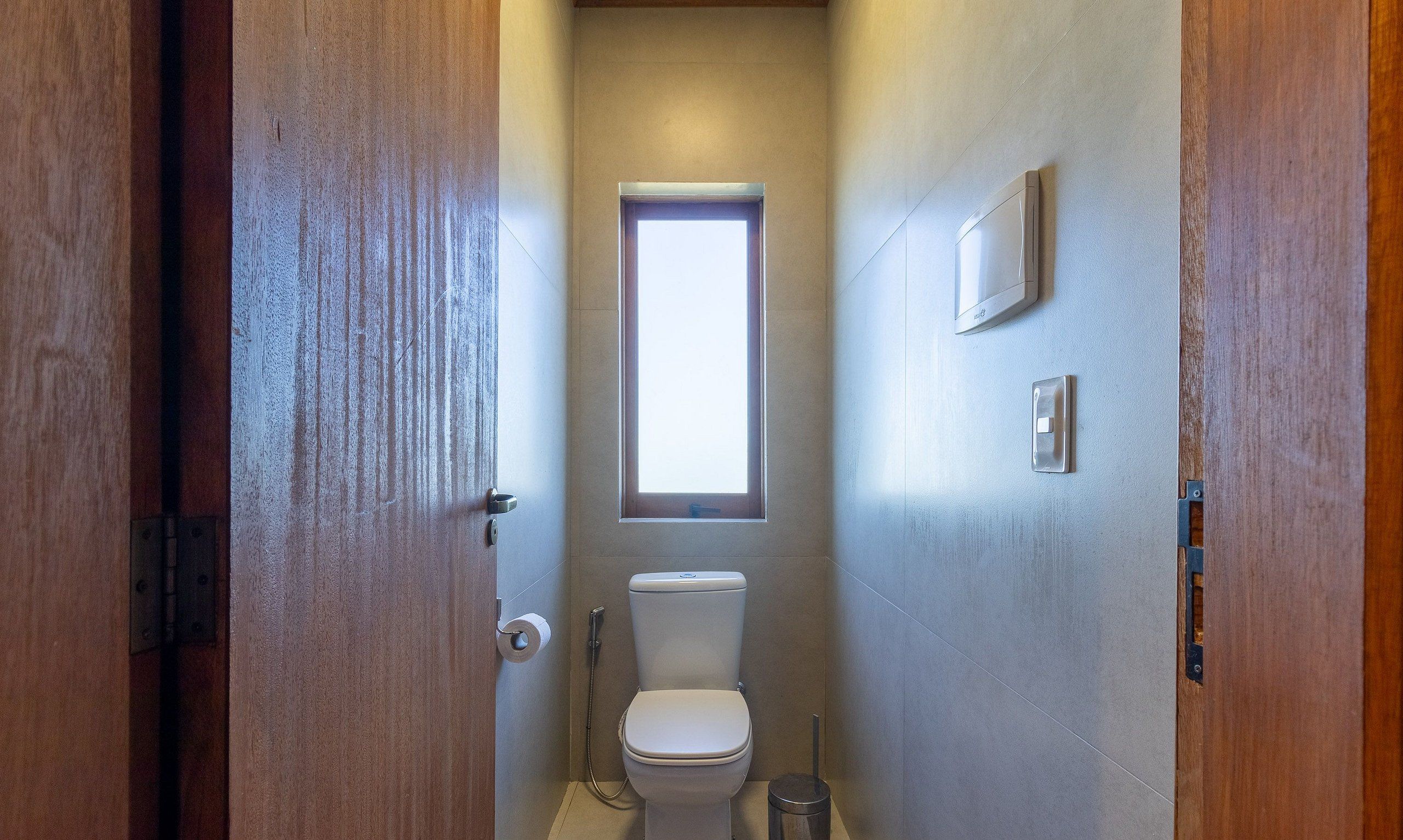 A narrow bathroom with a toilet, a window, and a shower.
