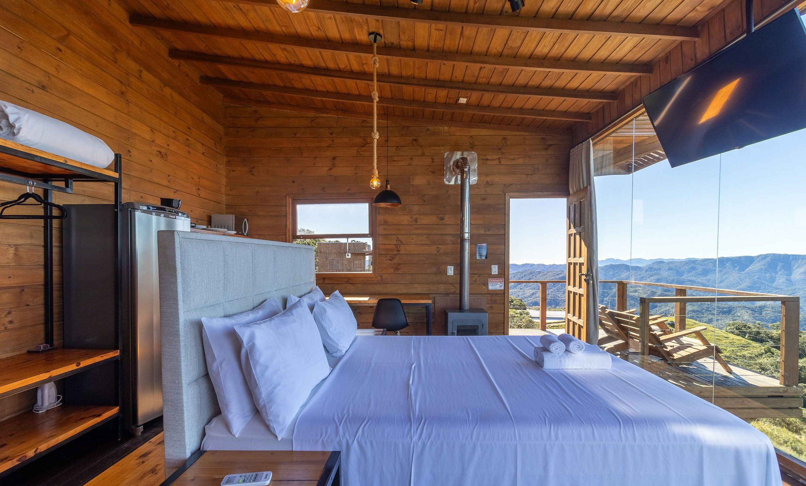 Un dormitorio de cabaña de madera con una cama, mesita de noche y vistas a las montañas.