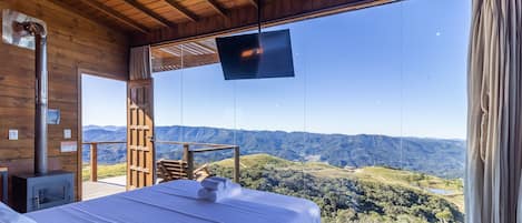 A room with a bed, a TV, and a view of a mountainous landscape.