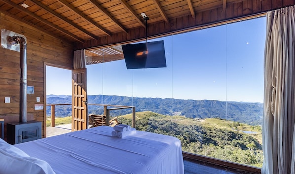 A room with a bed, a television, and a view of a mountainous landscape. - Linda cabana com jacuzzi VST004 (Anitapolis)
