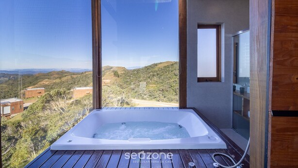 Un baño moderno con una bañera grande, suelo de madera y vistas al campo.