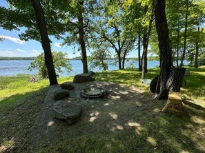 A campsite with a fire pit, a chair, and a view of a lake.