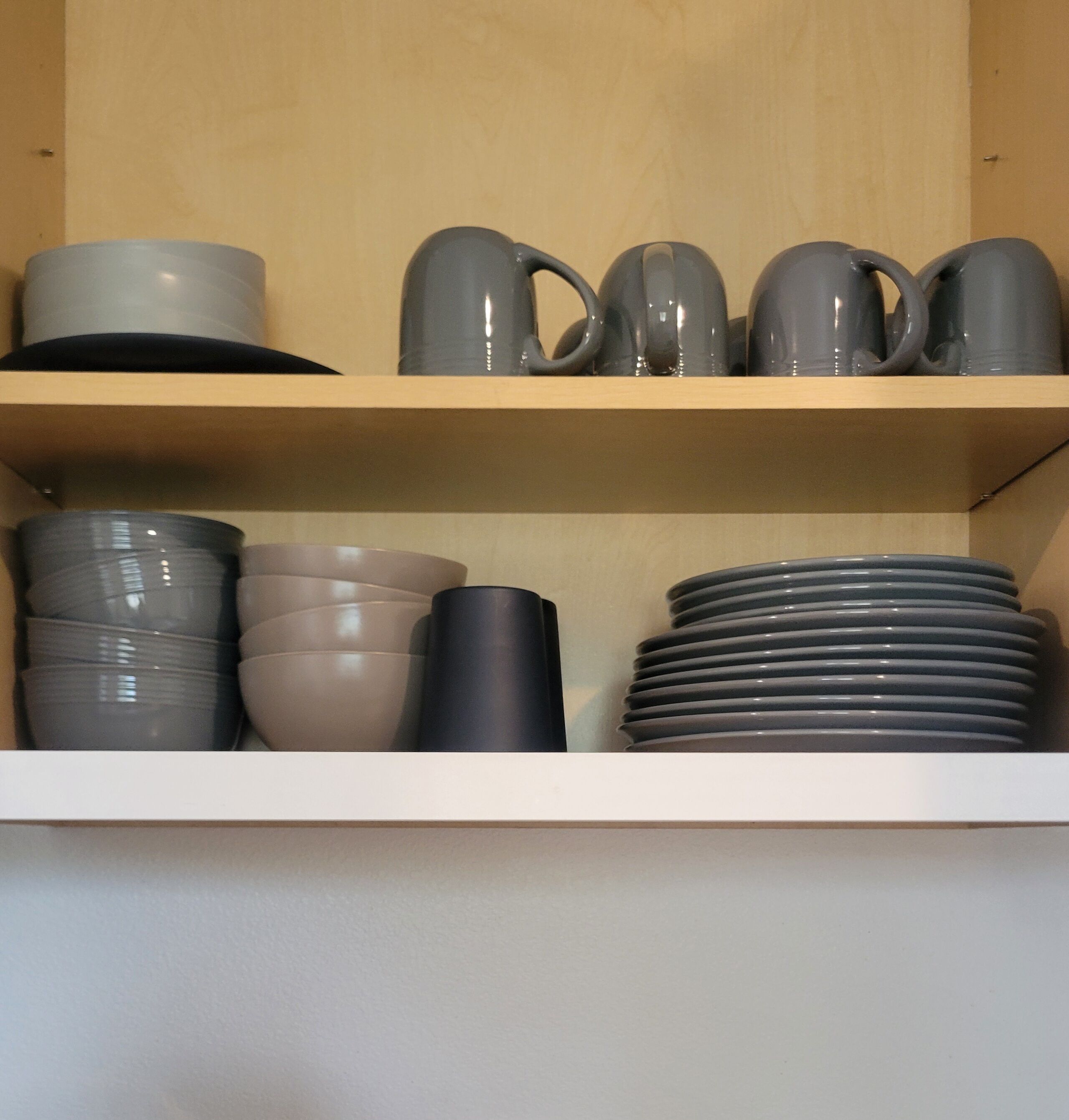 A shelf with various kitchenware including plates, bowls, and mugs.