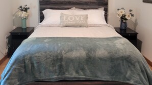 A bedroom with a dark wooden headboard, a bed with a grey blanket, two nightstands with flower vases, and a wall-mounted plant.