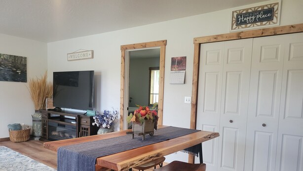 A dining area with a wooden table and bar stools, a television, and a welcome sign.