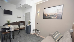 A modern living room with a sofa, a dining area with a table and chairs, a bed, and a TV mounted on the wall. - Crisvan Residence Igea Marina (Bellaria-Igea Marina)