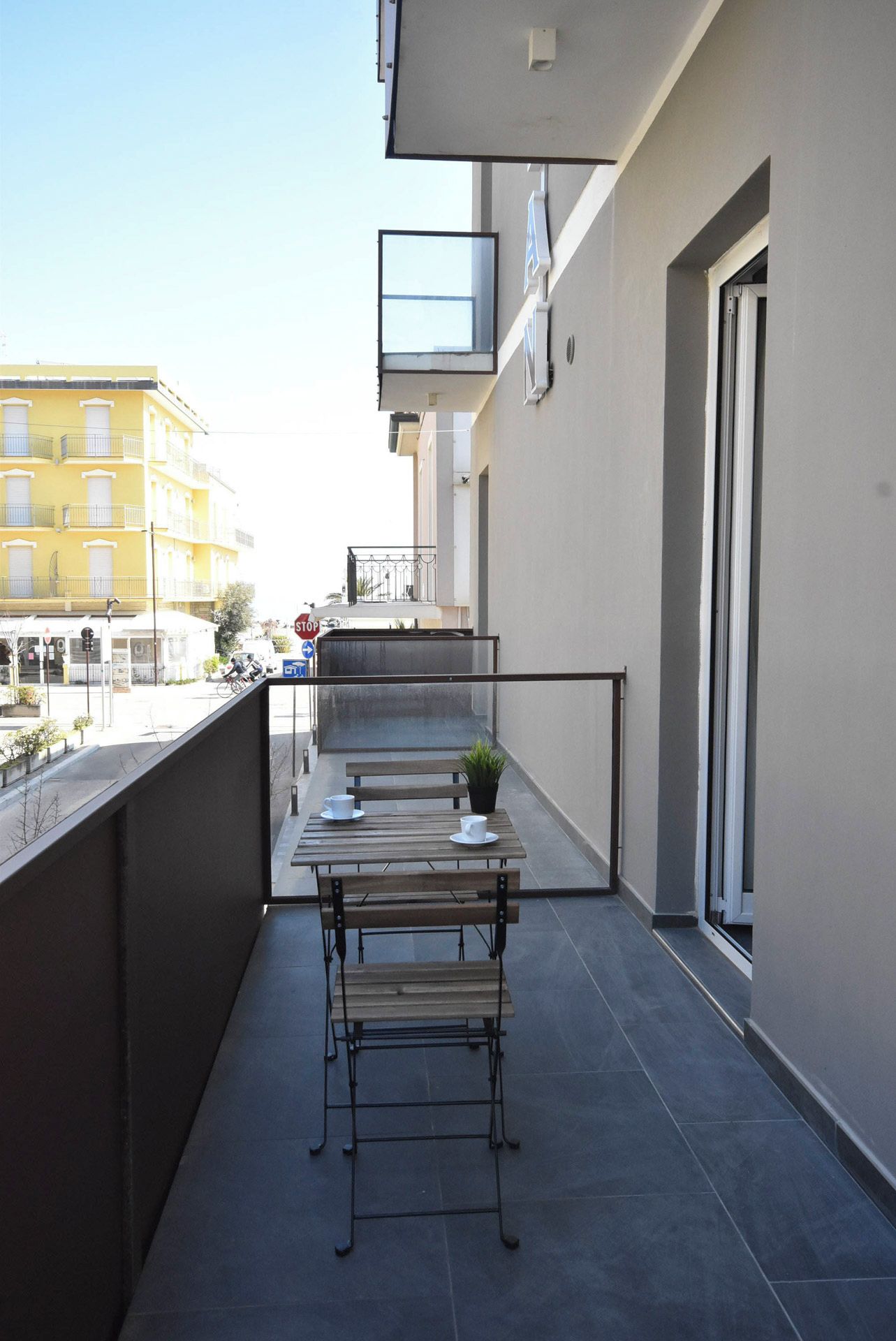 Ein Balkon mit Tisch und Stühlen, einem Blumentopf und Blick auf ein gelbes Gebäude.