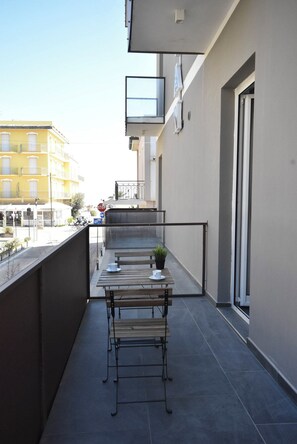 Un balcón con una mesa, sillas, una planta en maceta y vista a un edificio amarillo.