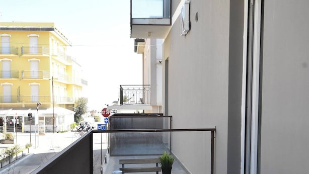 A balcony with a table and chairs, a potted plant, and a view of a yellow building. - Crisvan Residence Igea Marina (Bellaria-Igea Marina)
