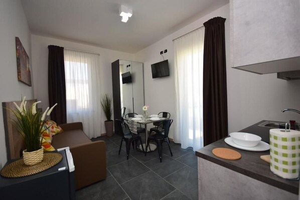 A modern living room with a sofa, dining table, chairs, and a kitchen area with a sink and counter.