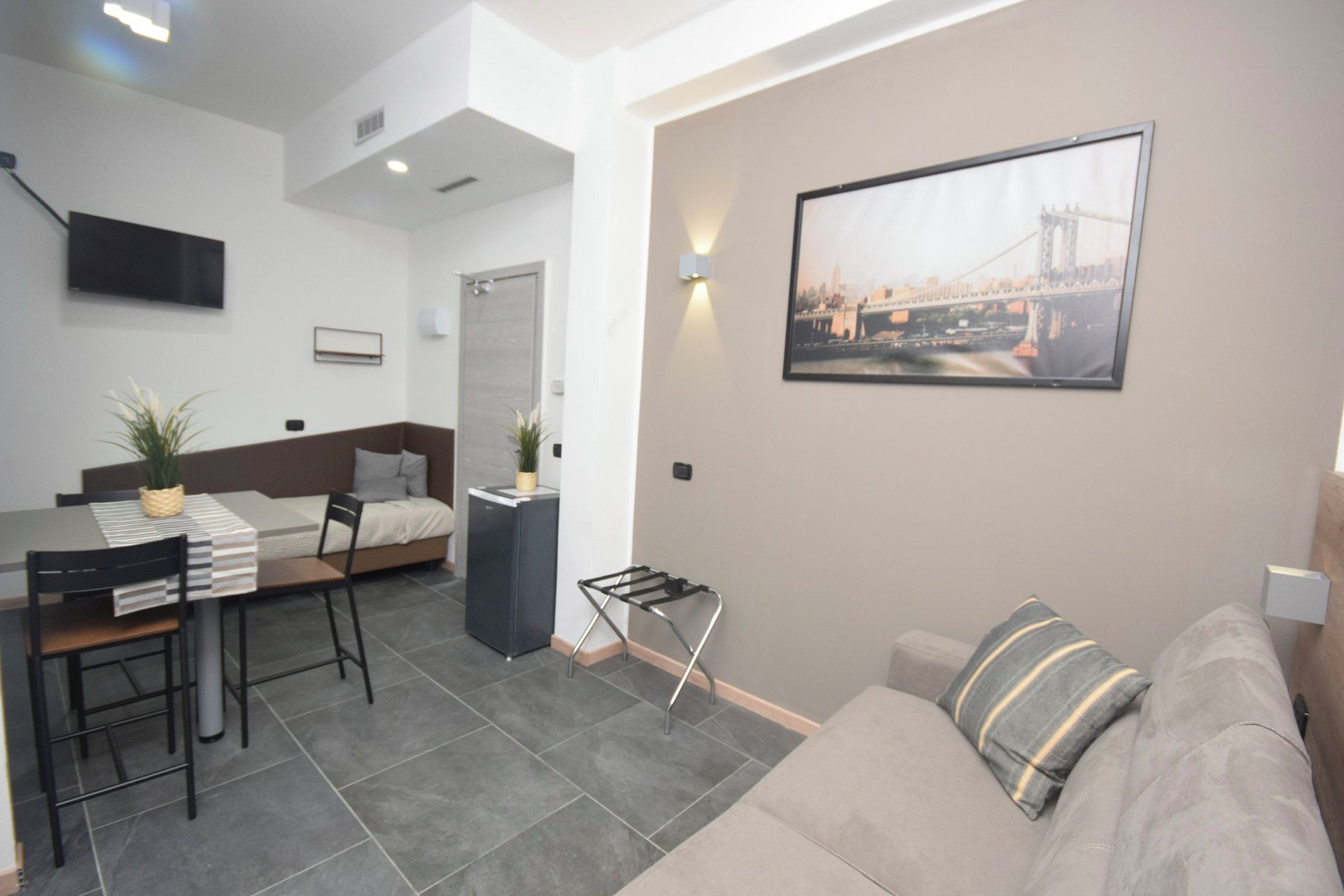 Een moderne woonkamer met een bank, een eethoek met een tafel en stoelen, een bed en een aan de muur bevestigde televisie.