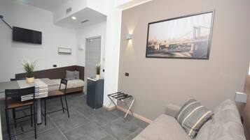 Een moderne woonkamer met een bank, een eethoek met een tafel en stoelen, een bed en een aan de muur bevestigde televisie.