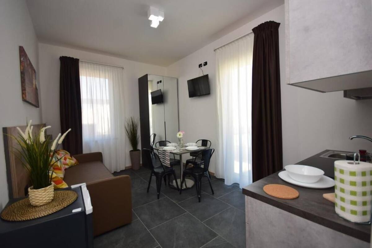 A modern living room with a sofa, dining table, chairs, and a kitchen area with a sink and counter.