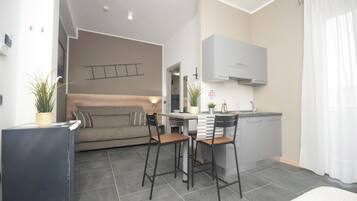 Een knus woongedeelte met een kitchenette, een bank, twee barkrukken en een eettafel.