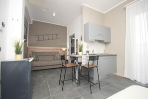 Un espacio habitable compacto con kitchenette, un sofá, dos taburetes altos y una mesa de comedor.