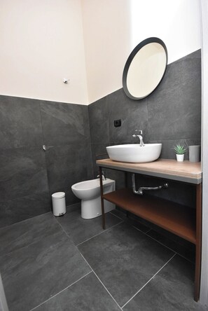 Une salle de bain moderne avec un lavabo blanc, un miroir rond et un bidet.