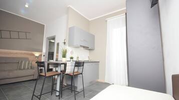 Een moderne, compacte leefruimte met een kitchenette, een eethoek en een groot bed.