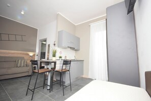 Un espacio habitable moderno y funcional con kitchenette, comedor y una cama grande.