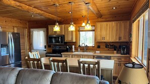 Interior acogedor de una cabaña con paredes de madera, un comedor, una cocina con electrodomésticos modernos y una zona de estar confortable.
