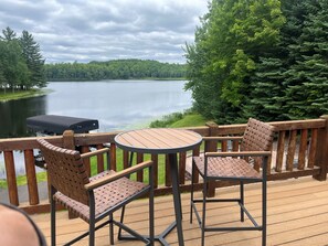 A deck with two chairs and a table overlooking a lake, surrounded by trees. - Beautiful, newly renovated log lakefront home, 3BD, 2 BA, high speed WiFi (Marenisco)
