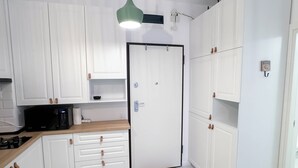 A modern kitchen with white cabinets, a microwave, and a green pendant light.