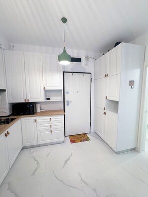 Une cuisine moderne avec des meubles blancs, un four à micro-ondes et un luminaire suspendu vert.