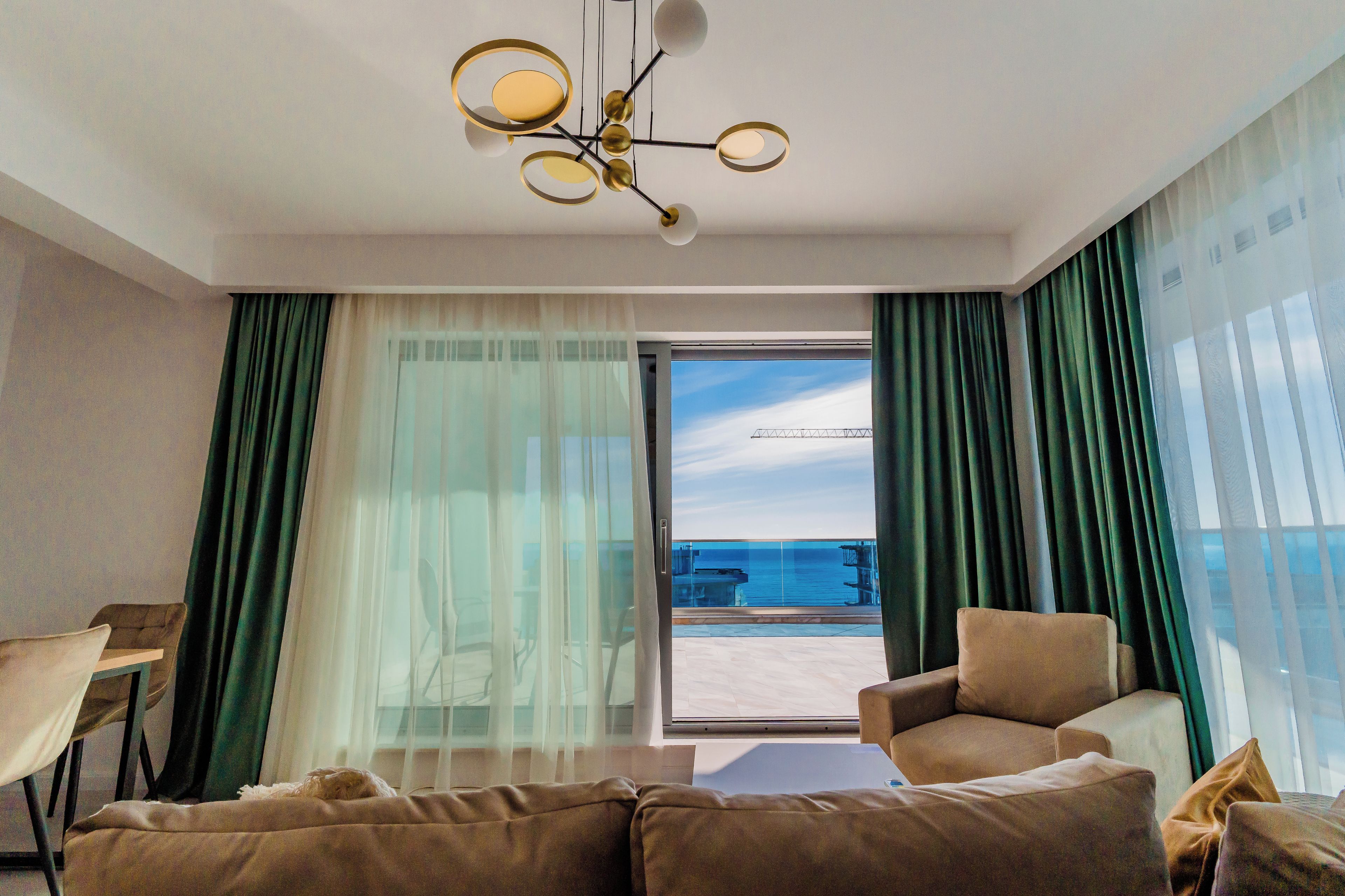 A modern hotel room with a large sliding glass door to the balcony, a sofa, a chair, and a table.