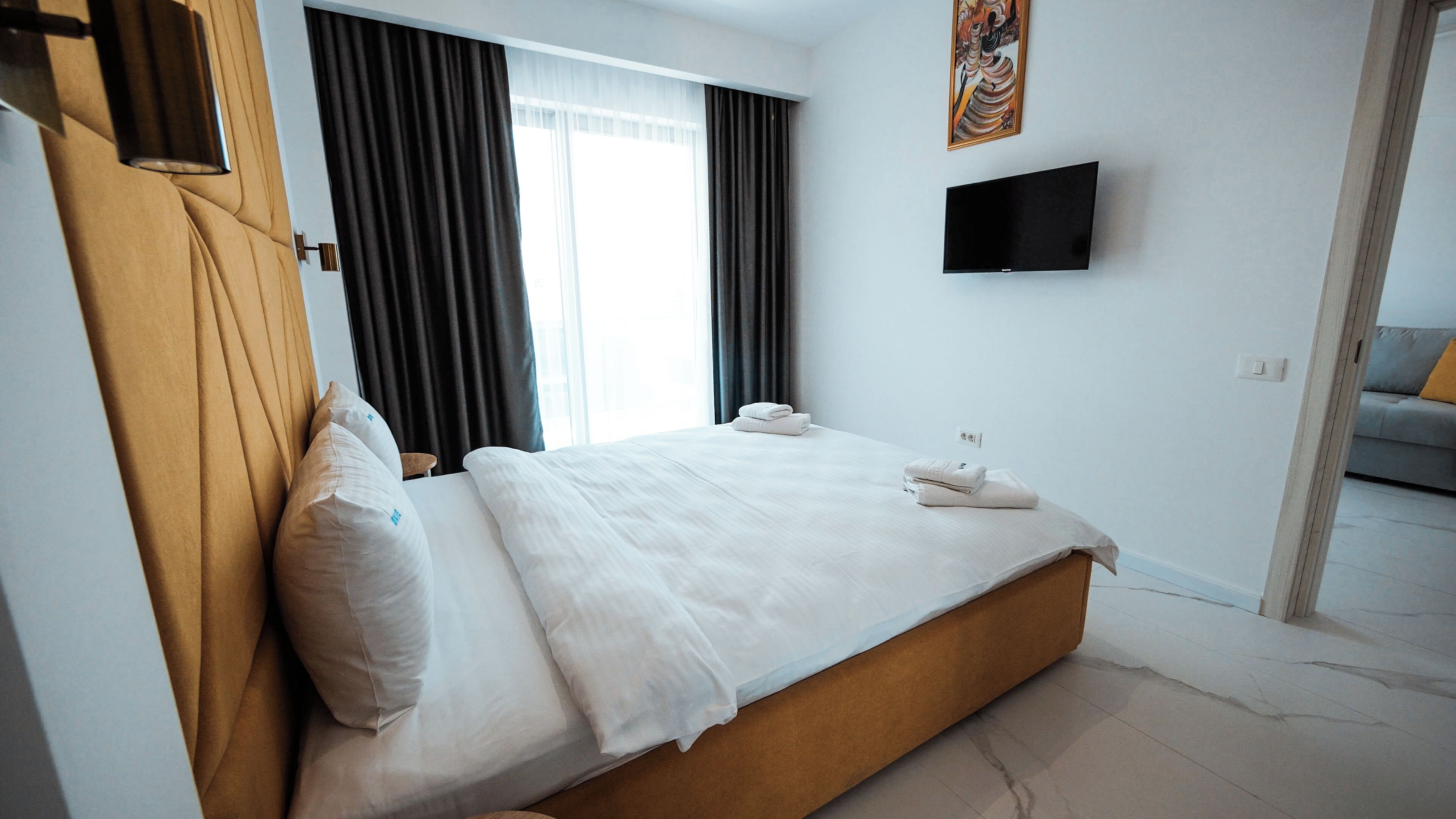 Une chambre d’hôtel avec un lit, un téléviseur à écran plat fixé au mur et une fenêtre avec des rideaux.