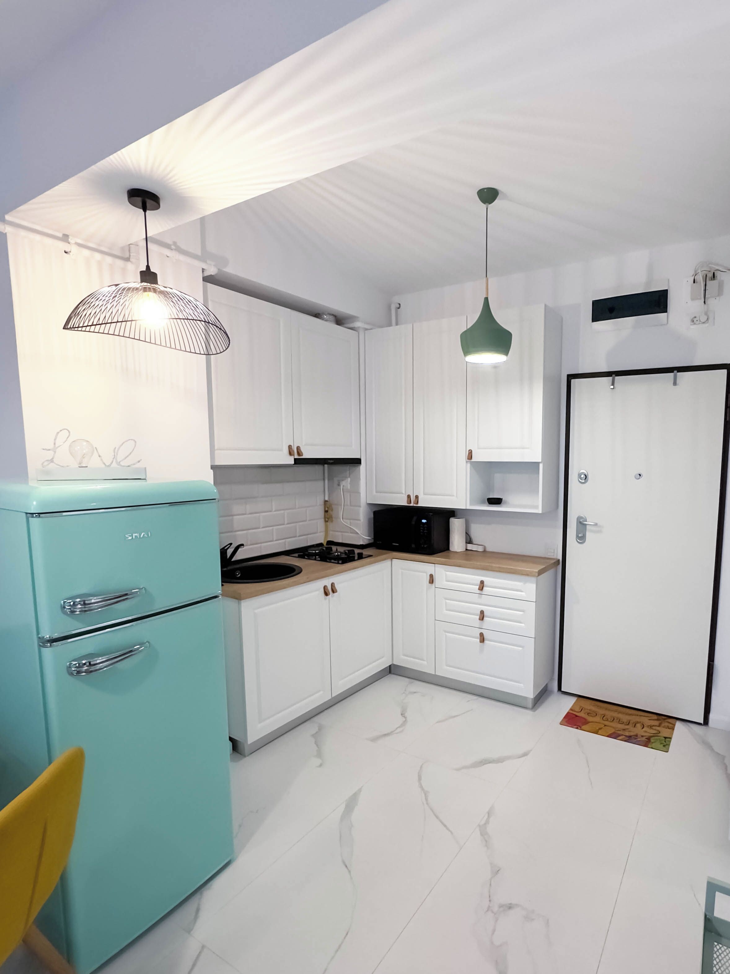 A kitchen with white cabinets, a teal refrigerator, a microwave, and a sink.