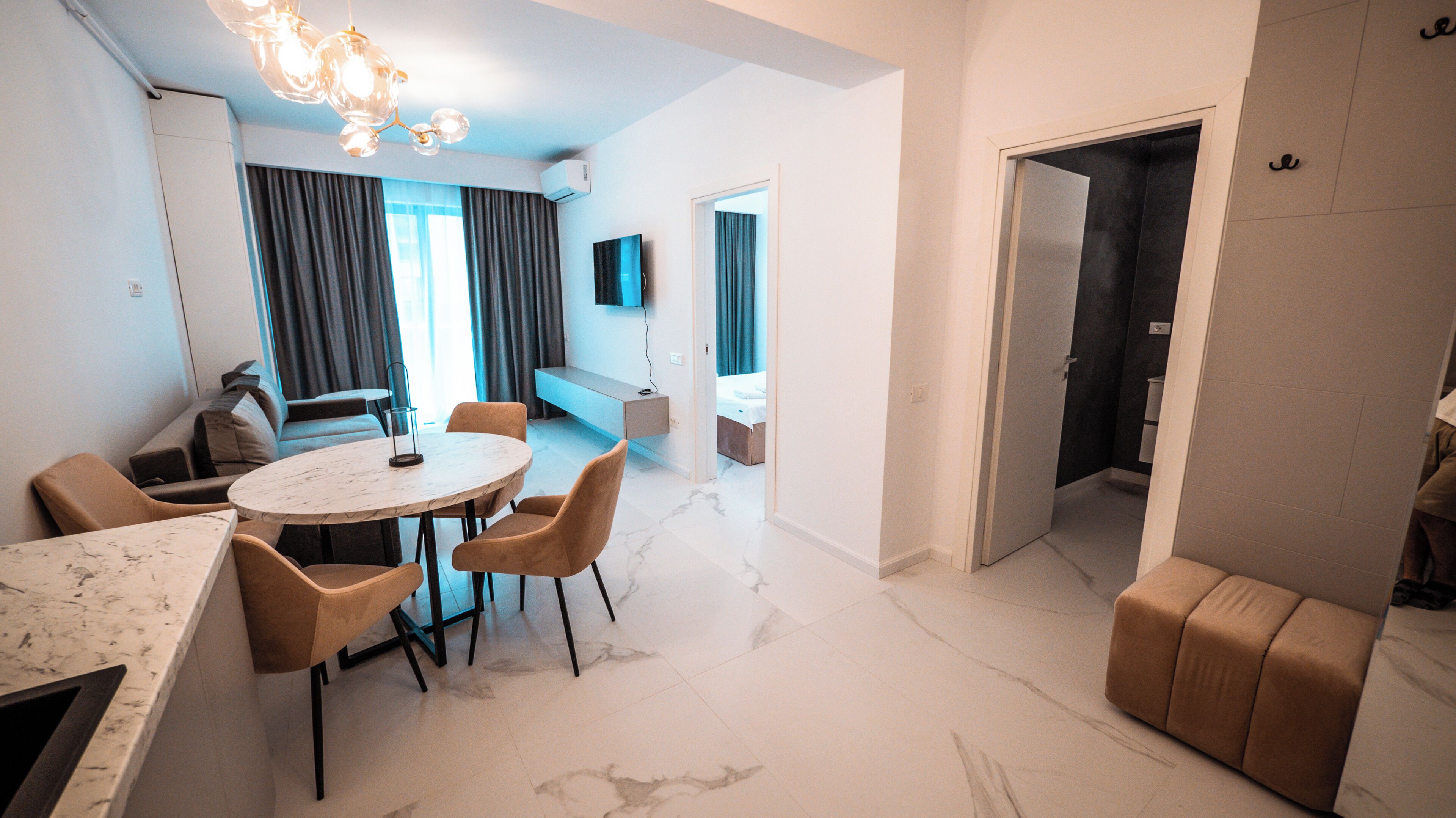 A modern living room with a marble floor, a round dining table with chairs, a sofa, and a TV mounted on the wall.