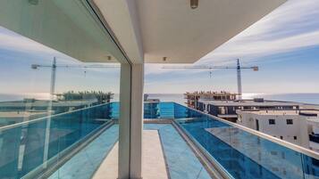 Eine moderne Dachterrasse mit Glasgeländern, einem Pool und Blick auf das Meer sowie Baukräne.