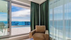 A modern room with a large sliding glass door leading to a balcony with a view of the sea and a bridge.