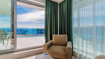 Ein modernes Zimmer mit einer großen Schiebeglastür, die auf einen Balkon mit Blick auf das Meer und eine Brücke führt.