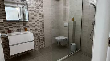Een moderne badkamer met een douchecabine van glas, een wastafel met spiegel en een toilet.