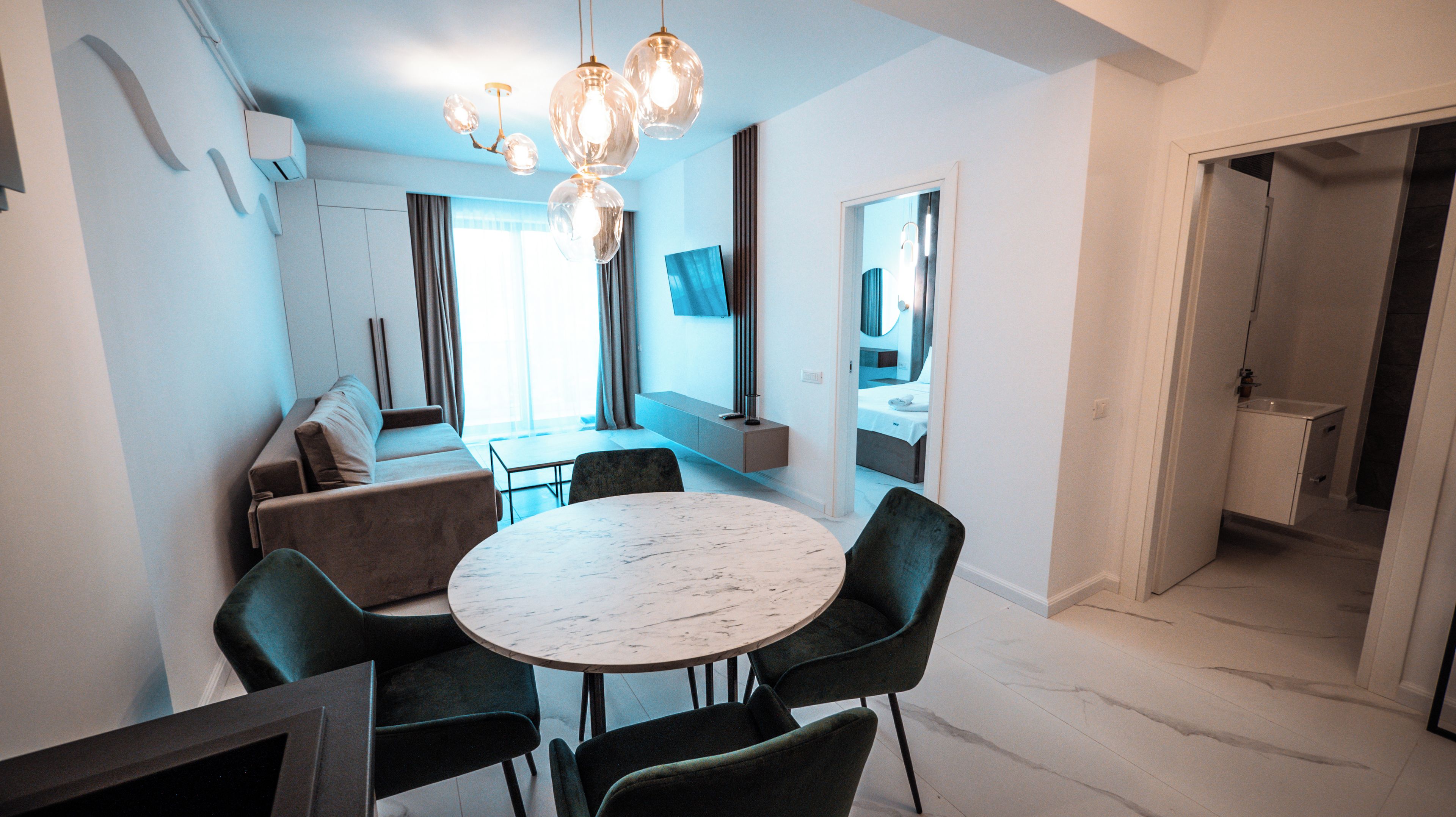 A modern dining area with a round table and chairs, a sofa, and a TV mounted on the wall.