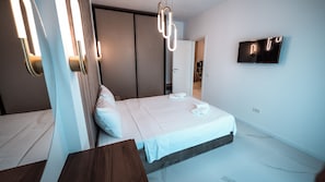 A modern hotel room with a bed, bedside tables, a TV, and a unique light fixture. - Wave 4 Apartments (Navodari)