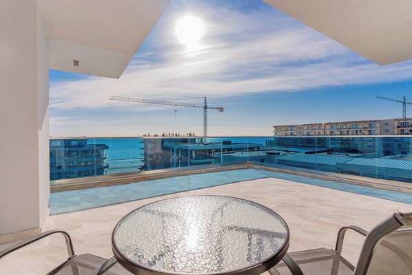 A rooftop terrace with a glass table and chairs, overlooking a construction site and a body of water. - Wave 4 Apartments (Navodari)