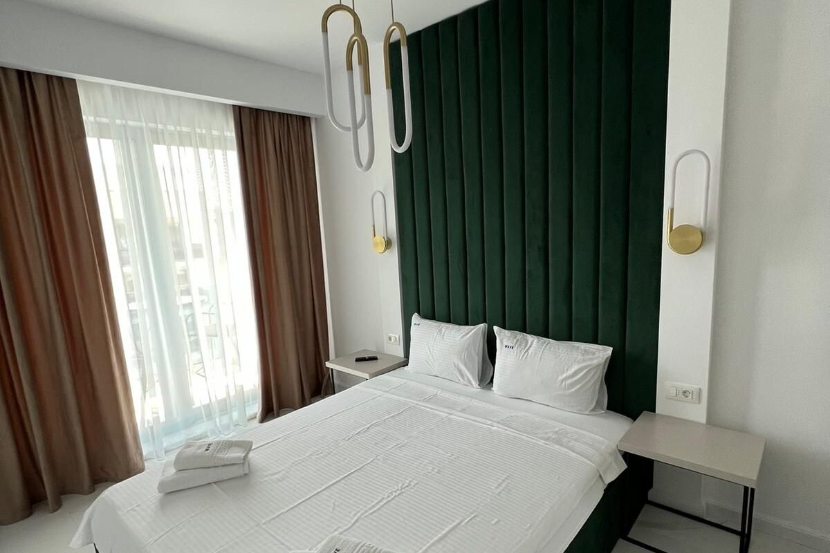 Une chambre d’hôtel avec un grand lit, une tête de lit verte, une table de chevet et une commode.