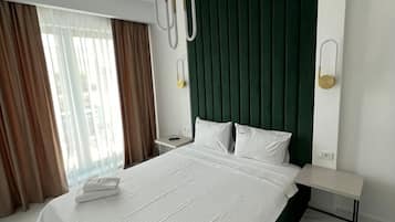 A hotel room with a large bed, a green headboard, a bedside table, and a nightstand.