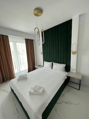 Et hotelværelse med en stor seng, et grønt sengegavl, et natbord og et lille bord ved siden af sengen.