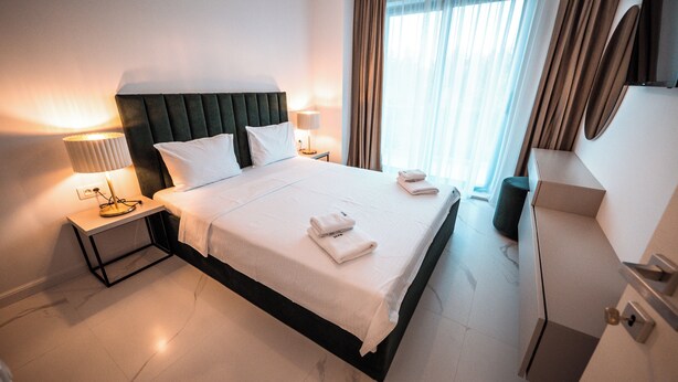 A hotel room with a large bed, two bedside tables with lamps, a dresser, and a window with curtains.