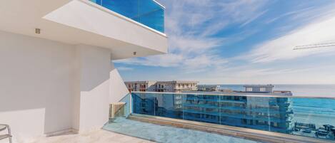 A modern balcony with a glass railing overlooking a body of water and buildings.