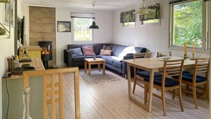 A cozy living room with a sofa, a dining table with chairs, a fireplace, and a window with curtains. - 3 bedroom cozy home in Vig (Vig)