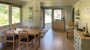 A spacious dining area with a wooden table and chairs, a kitchen with cabinets and a refrigerator, and a view of the outdoors through large windows. - 3 bedroom cozy home in Vig (Vig)