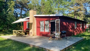A small red cabin with a wooden deck, a covered patio, and a grill. - 3 bedroom cozy home in Vig (Vig)