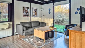 A modern living room with a sofa, a coffee table, a TV, and a window with a view of trees.